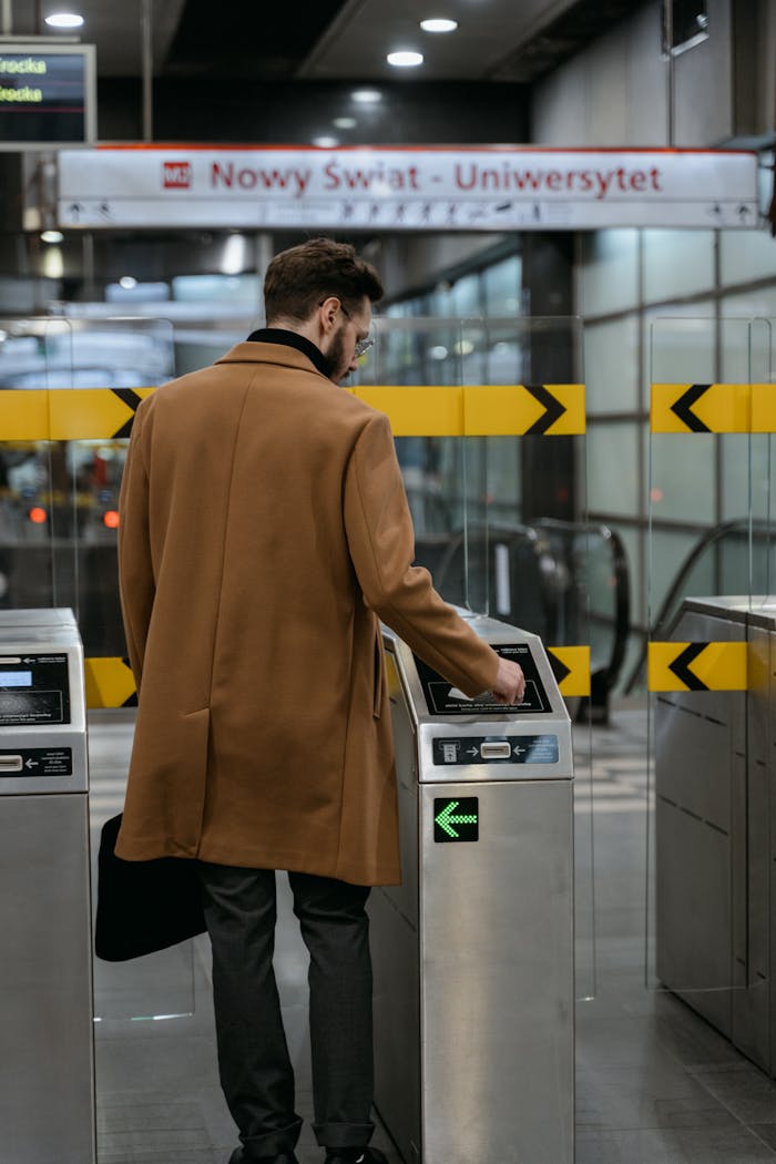 Back view of a man in a brown coat using a ticket barrier at a subway station.